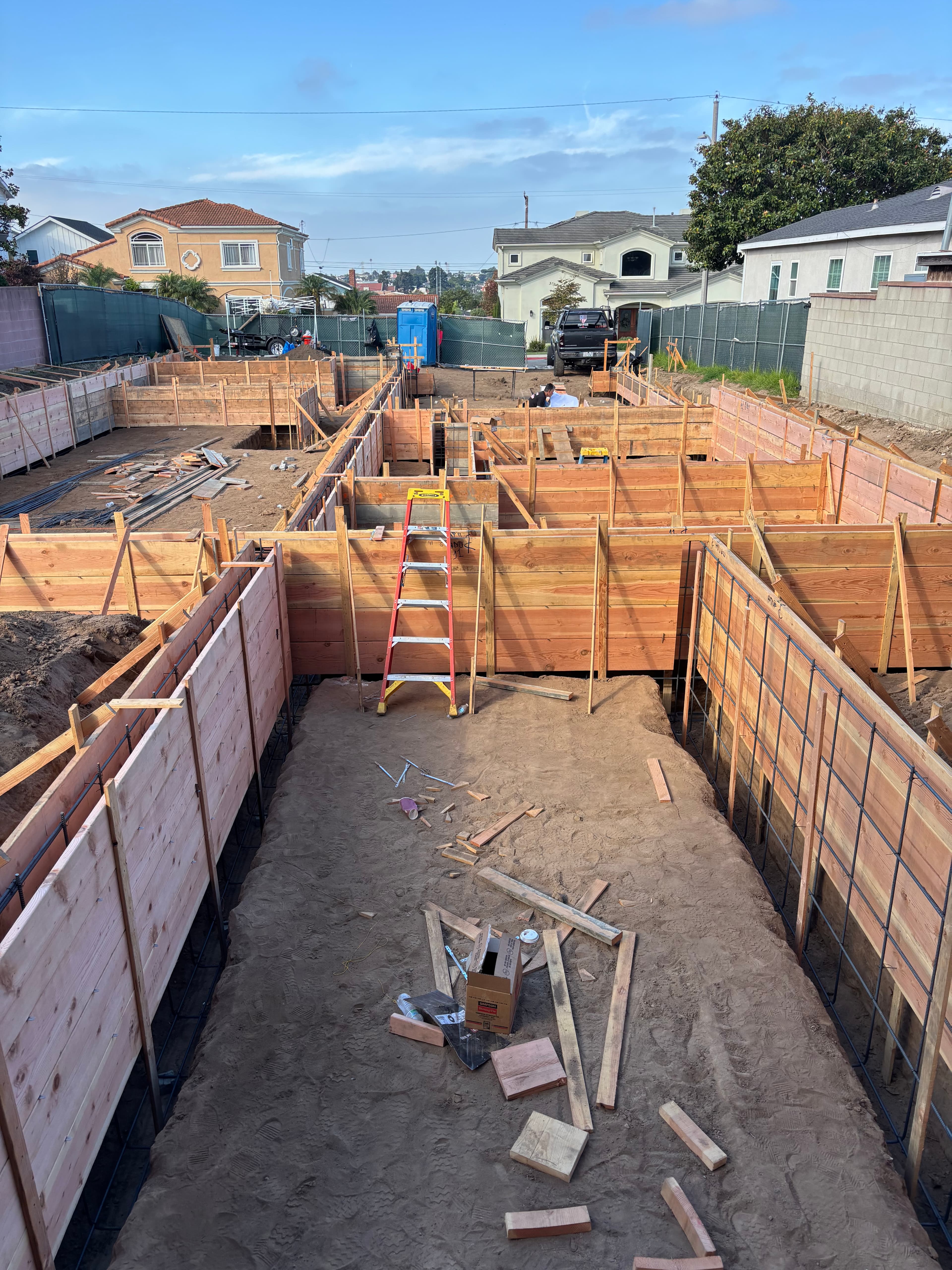 Wooden foundation forms and rebar at a residential construction site with a red ladder.