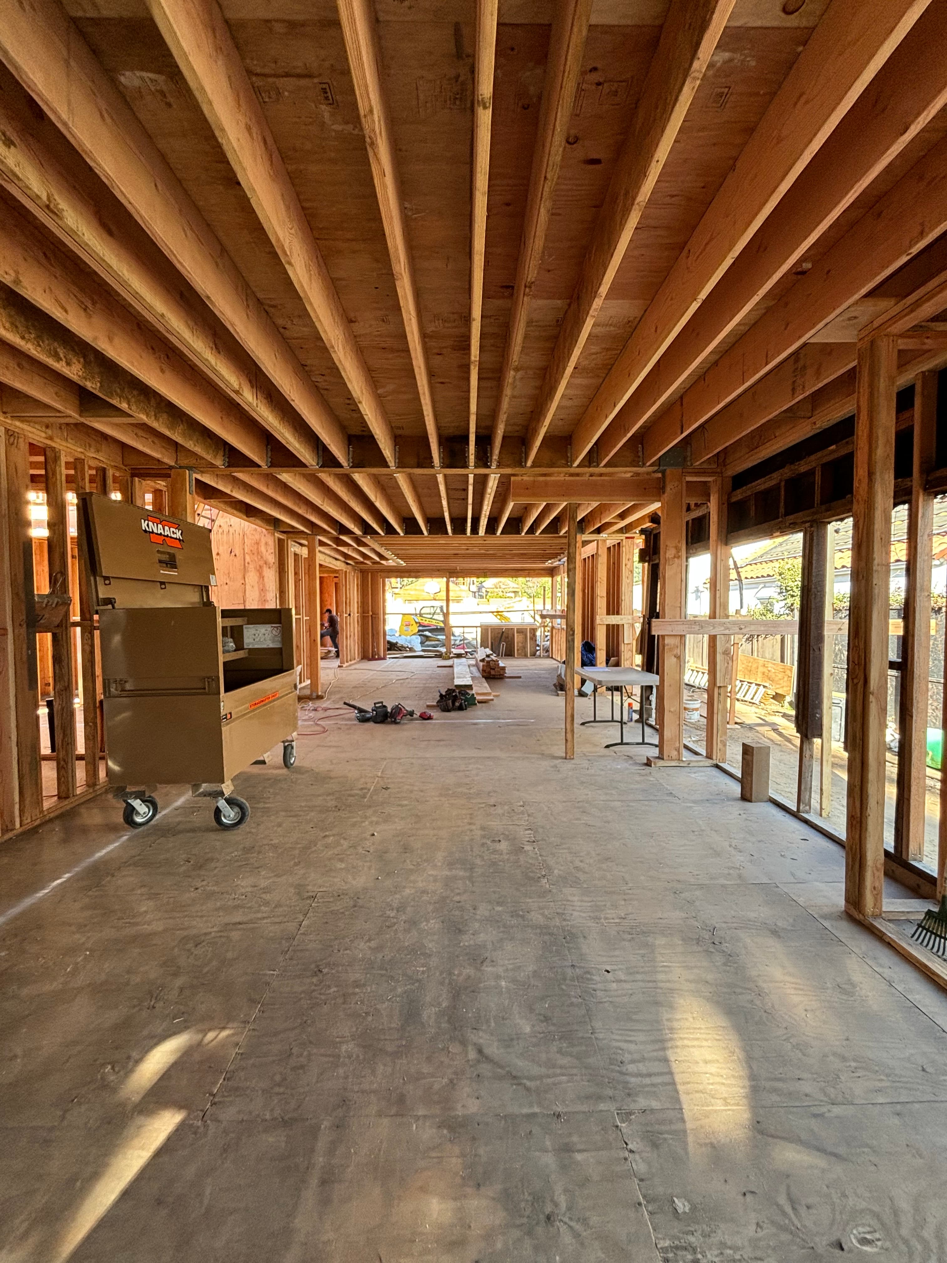 Interior construction site with wooden framing, ceiling joists, and a large tan tool chest.