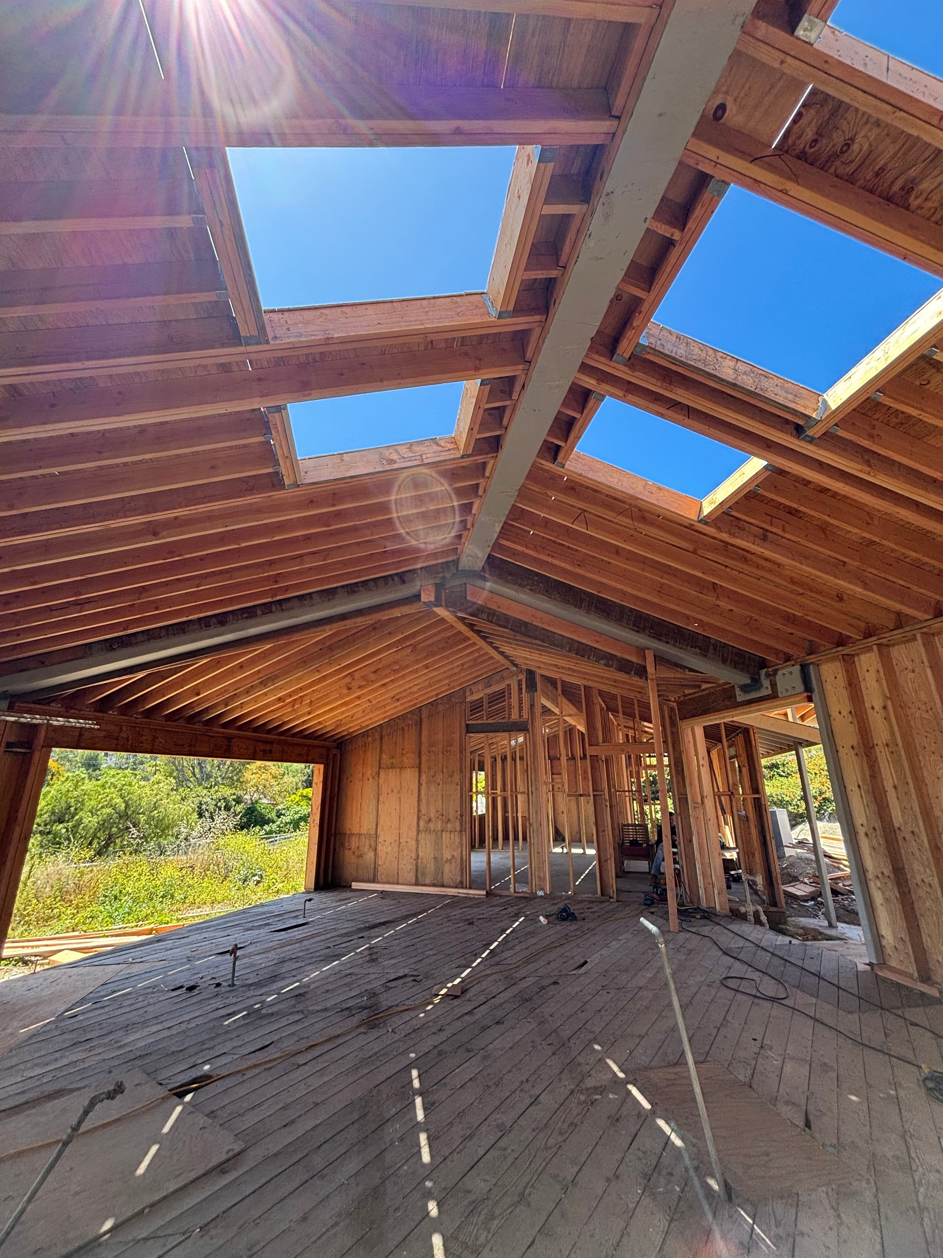Interior of a wooden house under construction with sunlight streaming through large roof skylight openings.